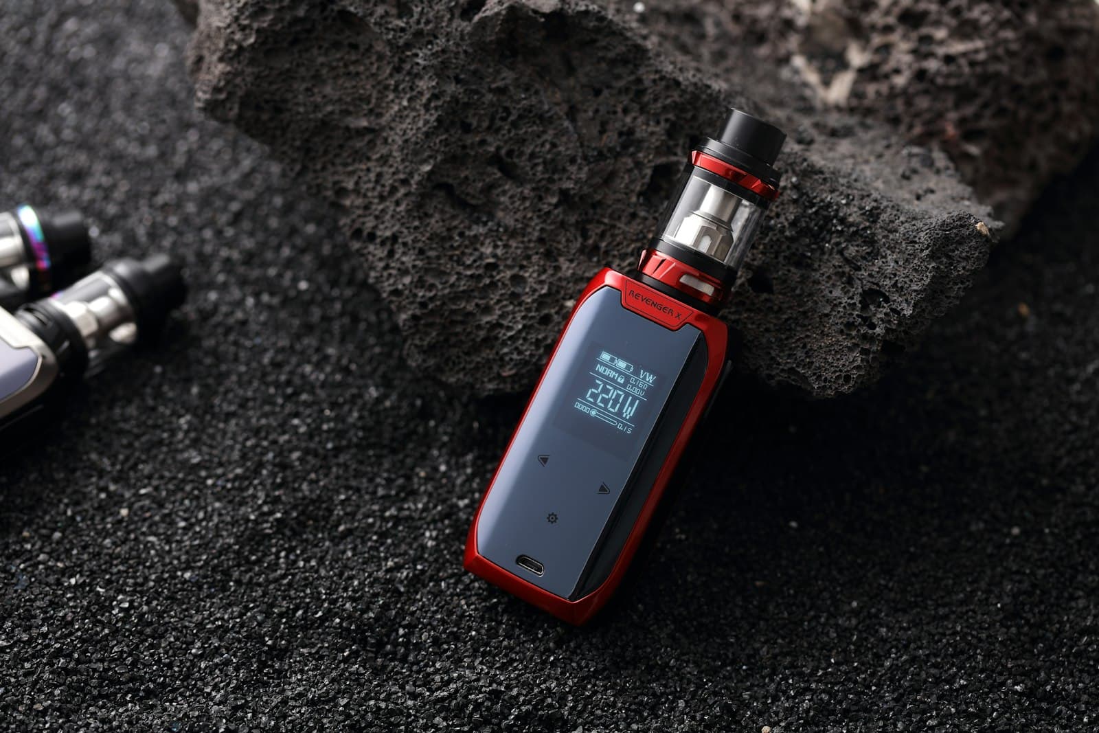Red and black vape mod with sub-ohm tank and adjustable airflow slots resting on dark volcanic rock