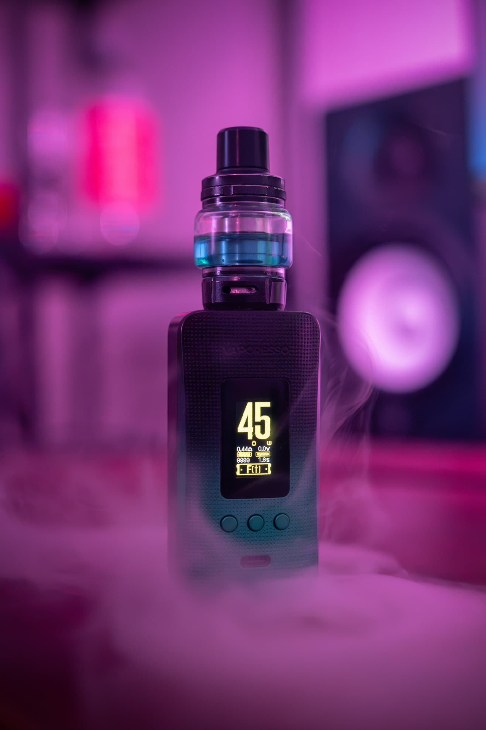 Vape mod digital display screen glowing with wattage and resistance readout in a smoke-filled purple-lit room